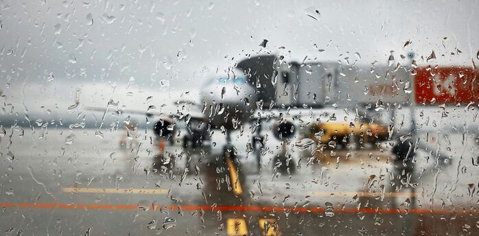 Rain-covered terminal window with aircraft visible on the tarmac