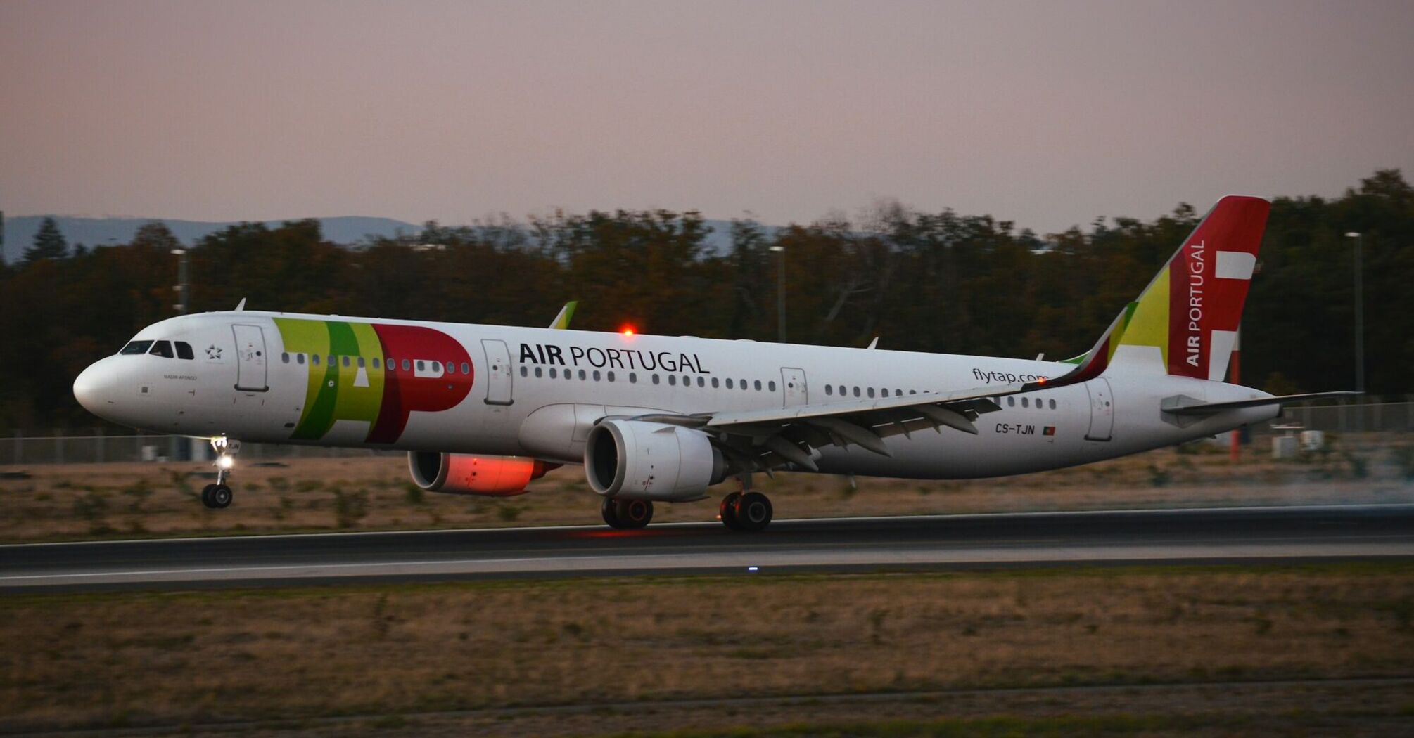 Air Portugal aircraft touching down on the runway at dusk