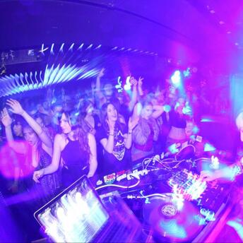 Crowded nightclub with a DJ performing under bright purple and blue lights