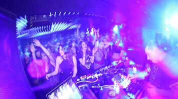 Crowded nightclub with a DJ performing under bright purple and blue lights