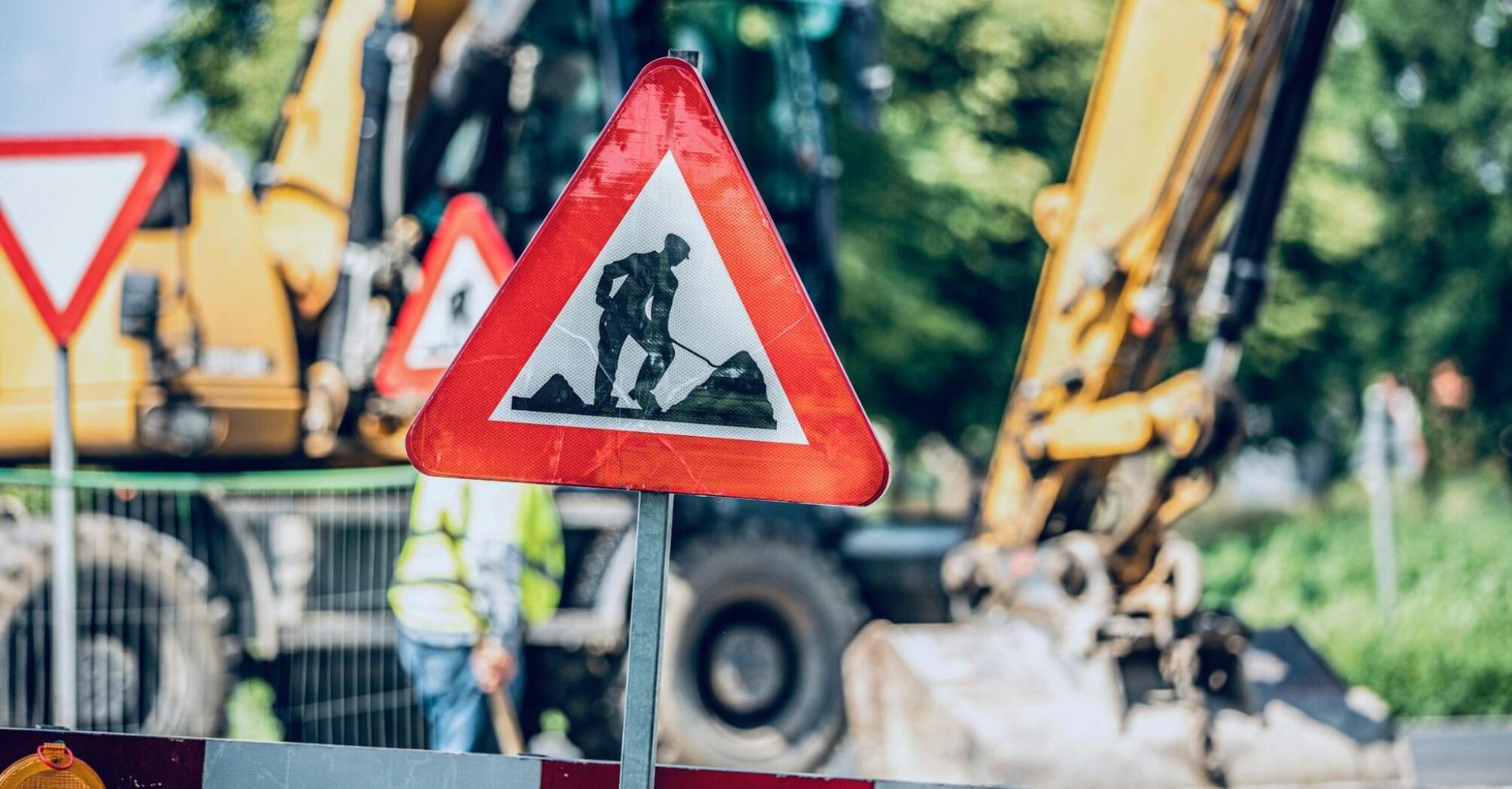 Roadwork sign placed near active construction machinery on a blocked street