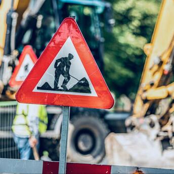 Roadwork sign placed near active construction machinery on a blocked street