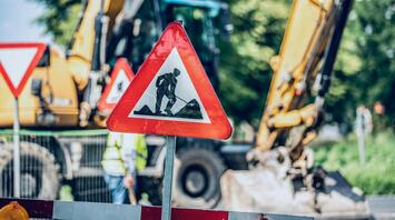 Roadwork sign placed near active construction machinery on a blocked street