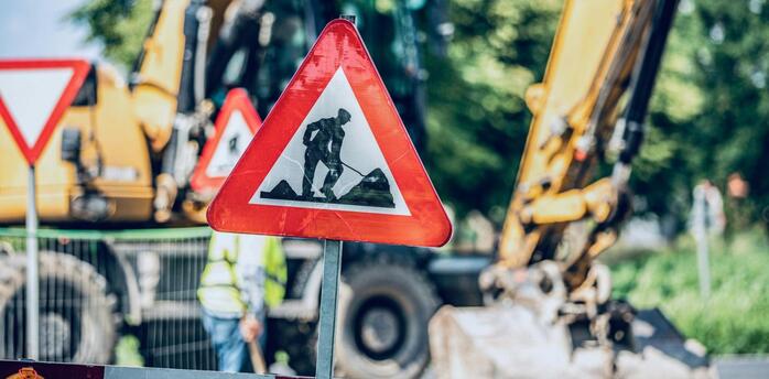 Roadwork sign placed near active construction machinery on a blocked street