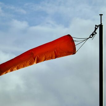 Orange windsock blowing strongly against cloudy sky