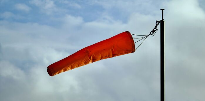 Orange windsock blowing strongly against cloudy sky