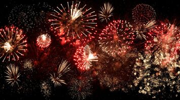 Multiple red and gold fireworks bursting in the night sky