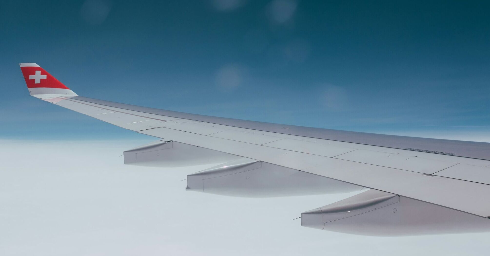 Wing of a SWISS aircraft flying above cloud cover