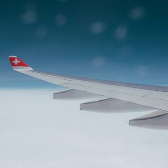 Wing of a SWISS aircraft flying above cloud cover