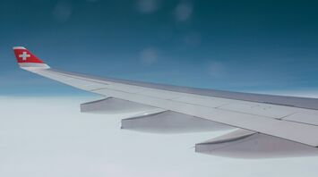 Wing of a SWISS aircraft flying above cloud cover