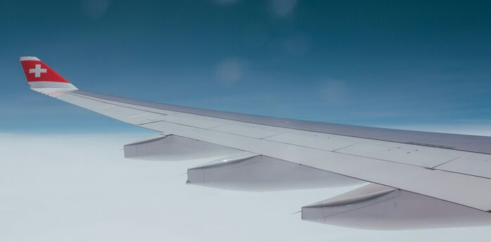 Wing of a SWISS aircraft flying above cloud cover