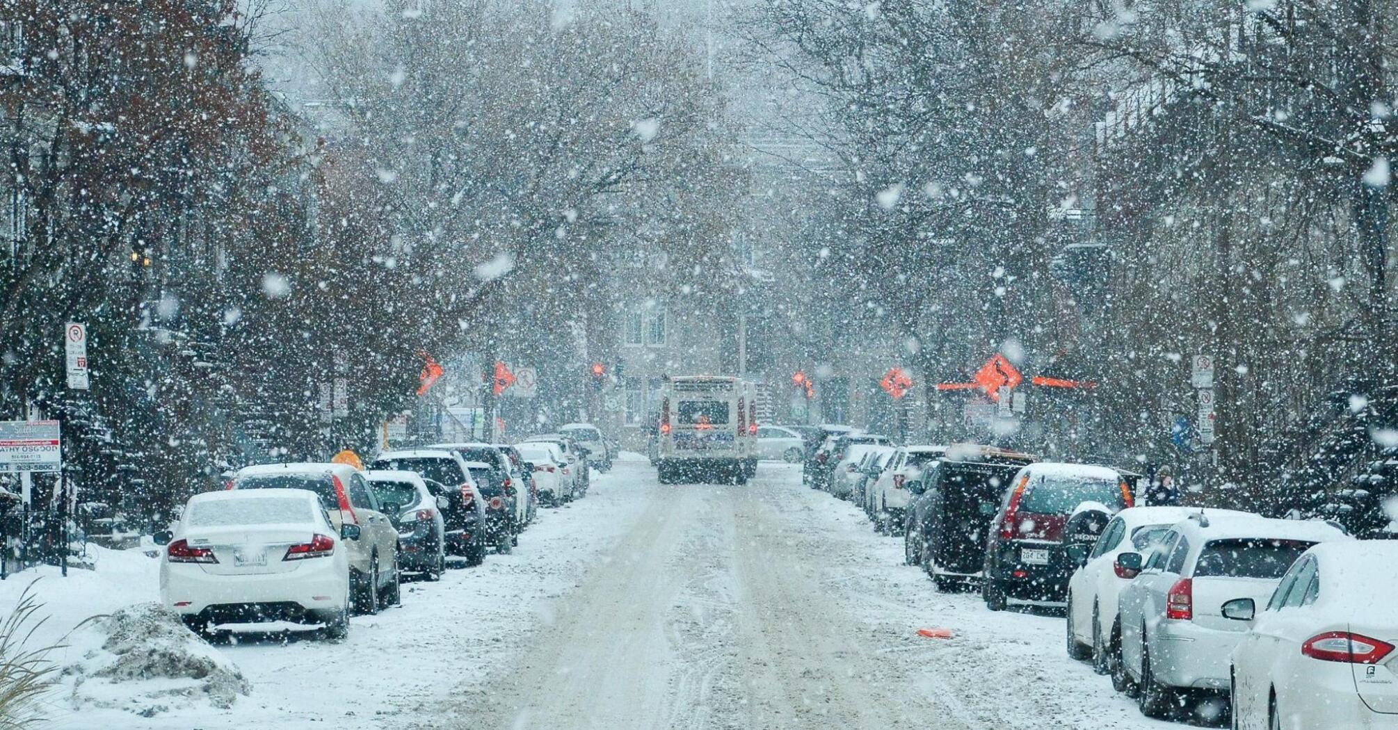 Snow-covered street with parked cars and limited visibility during heavy snowfall