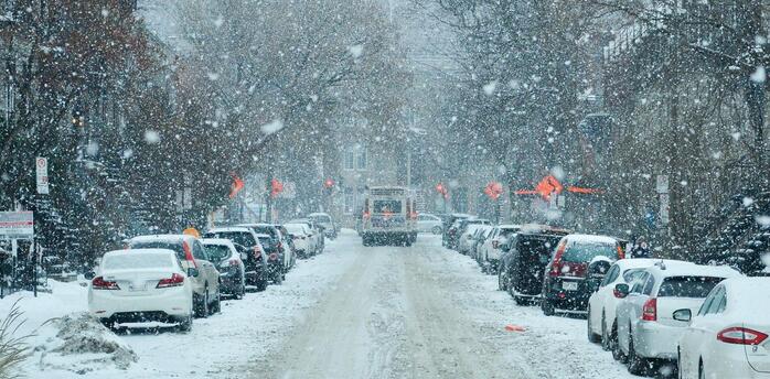 Snow-covered street with parked cars and limited visibility during heavy snowfall