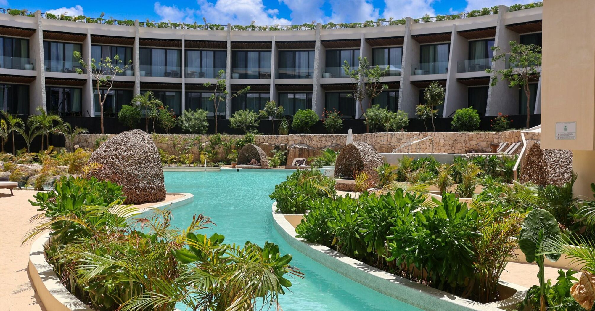 Resort pool surrounded by tropical plants and guest suites