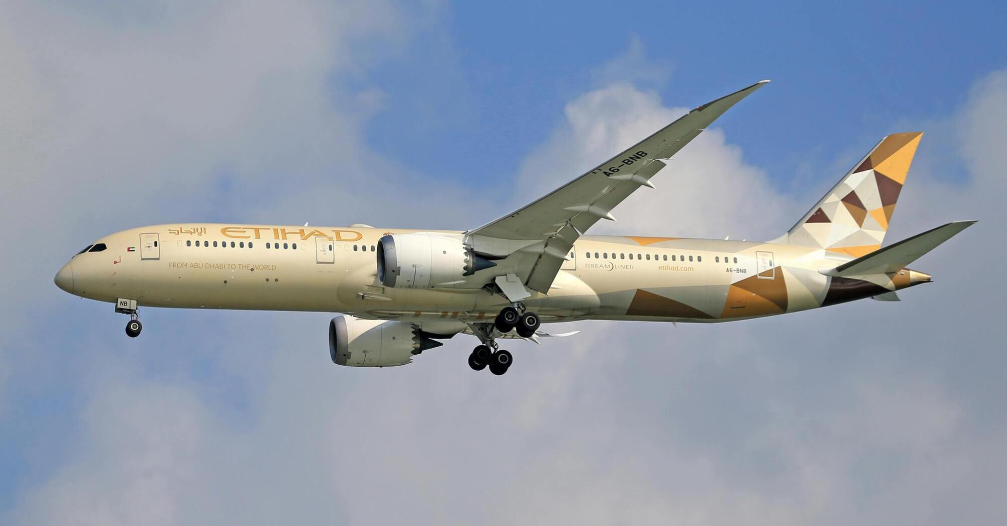 Etihad Airways plane in flight with landing gear deployed against a cloudy sky