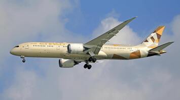 Etihad Airways plane in flight with landing gear deployed against a cloudy sky