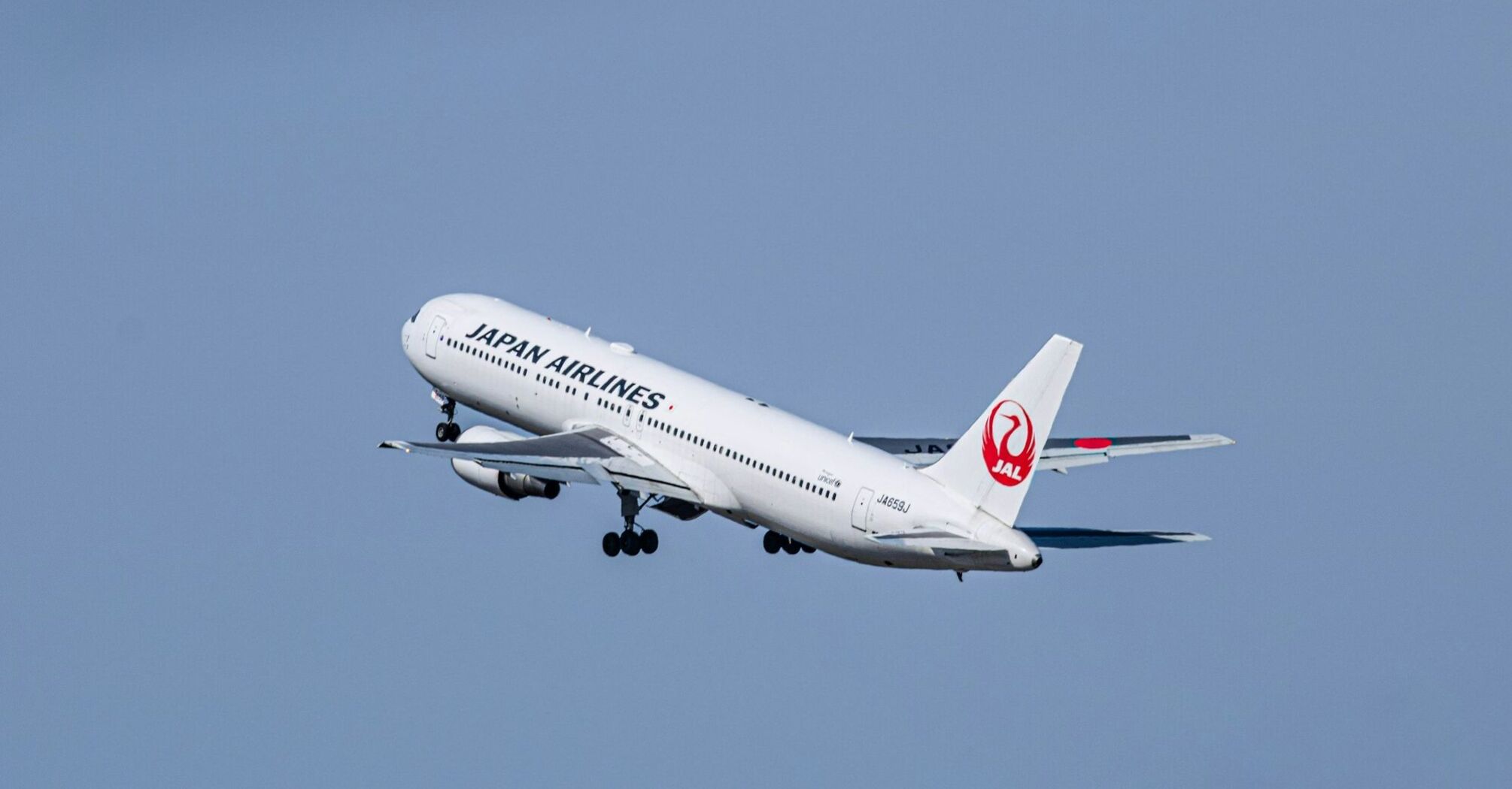 A Japan Airlines (JAL) aircraft taking off against a clear blue sky