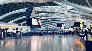 A modern, spacious terminal at Heathrow Airport with check-in kiosks, passengers, and illuminated signage