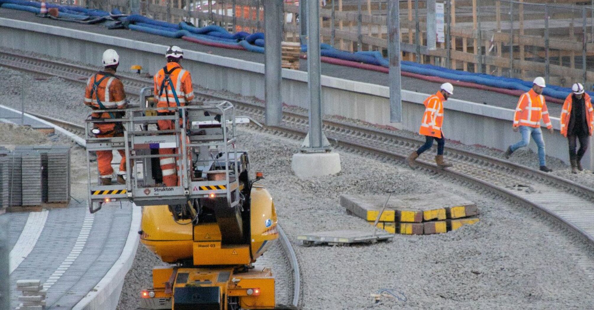 Railway workers in high-visibility clothing performing track maintenance with specialized equipment at a construction site