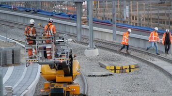 Railway workers in high-visibility clothing performing track maintenance with specialized equipment at a construction site