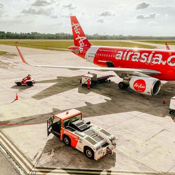 AirAsia aircraft on the tarmac with ground crew and support vehicles at an airport