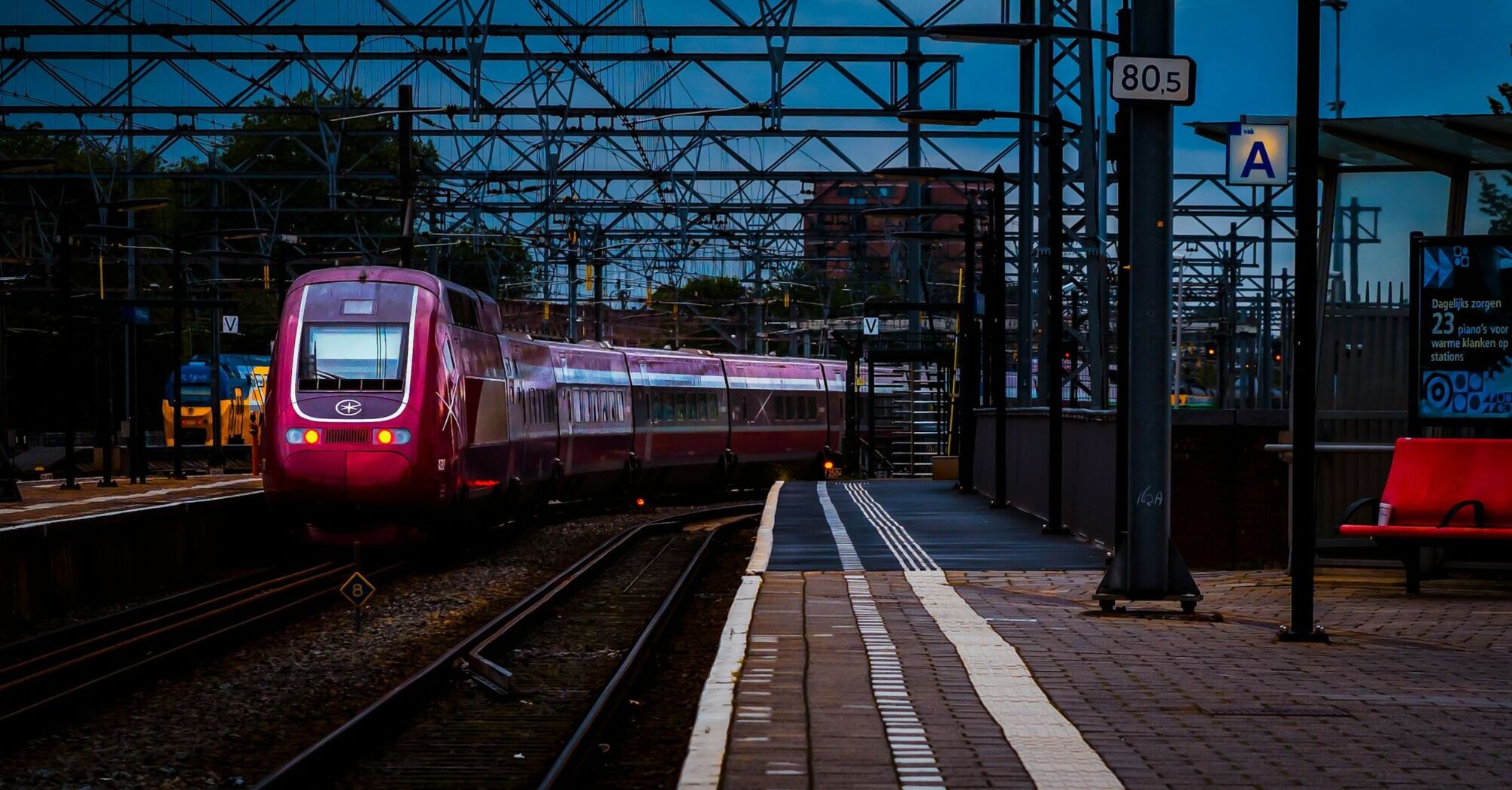 A modern Eurostar train at a Amsterdam railway station under overhead electric lines during twilight