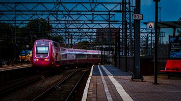 A modern Eurostar train at a Amsterdam railway station under overhead electric lines during twilight
