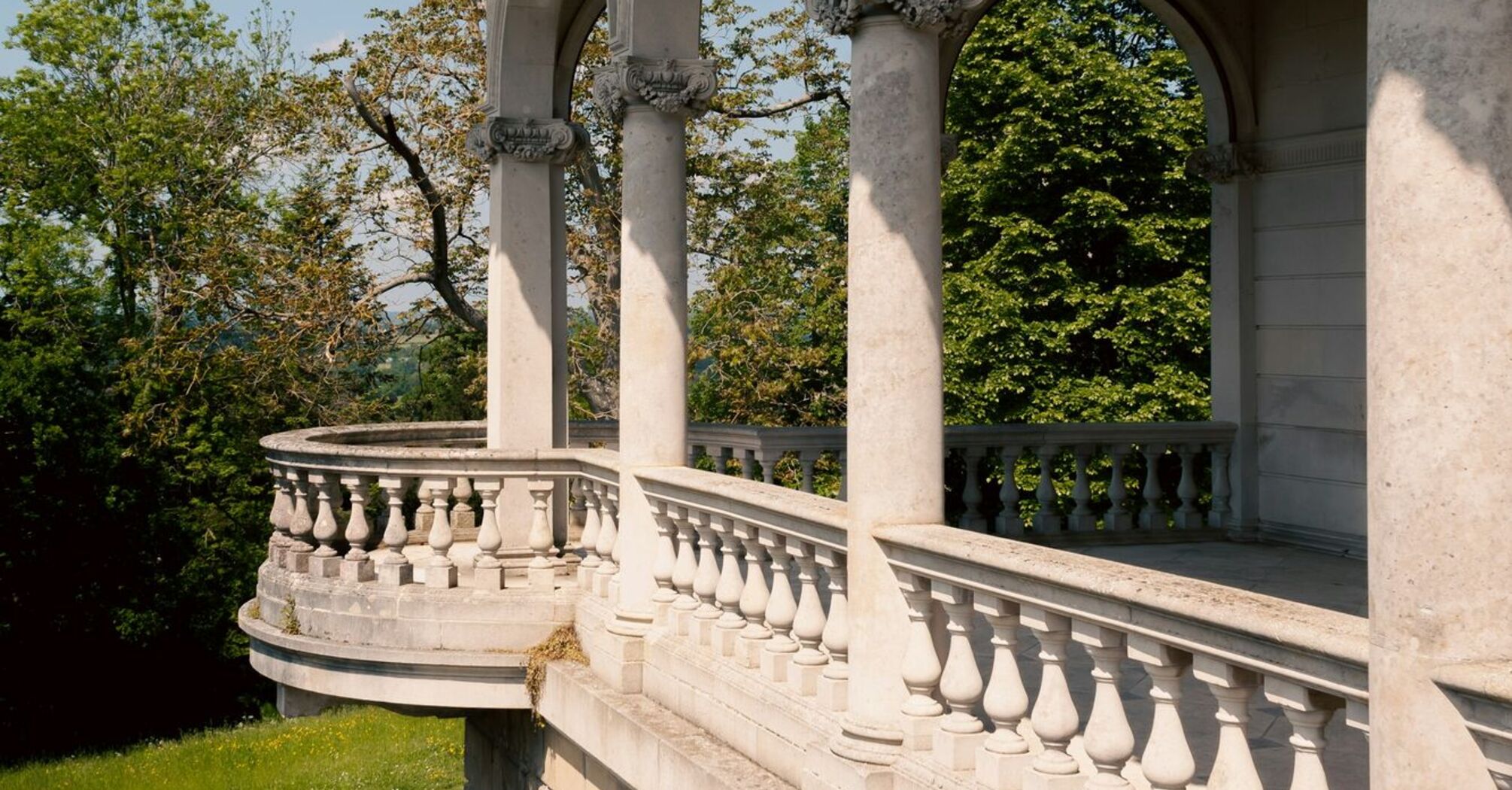 A historic stone terrace with elegant arches and balustrades overlooking lush greenery