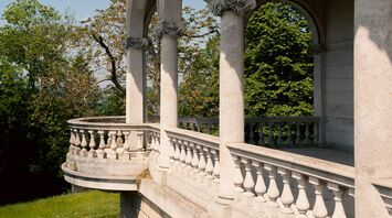 A historic stone terrace with elegant arches and balustrades overlooking lush greenery