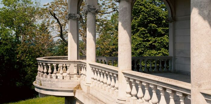 A historic stone terrace with elegant arches and balustrades overlooking lush greenery