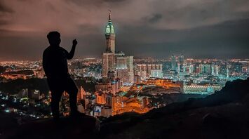 Silhouette of a person overlooking the illuminated skyline of Makkah at night, featuring the Abraj Al Bait Towers and the Grand Mosque