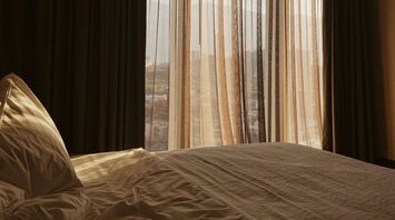 A cozy hotel room with sunlight filtering through sheer curtains, overlooking a cityscape