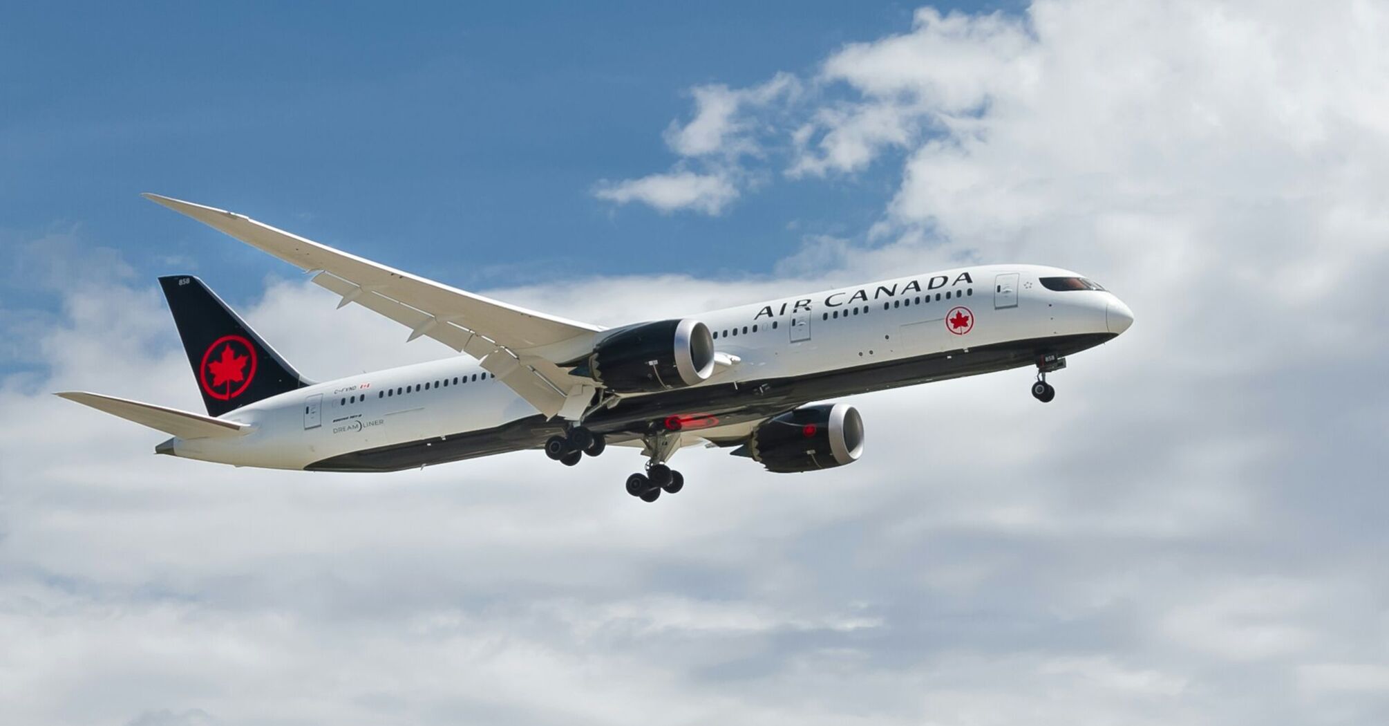 Air Canada airplane in flight against a blue sky with clouds