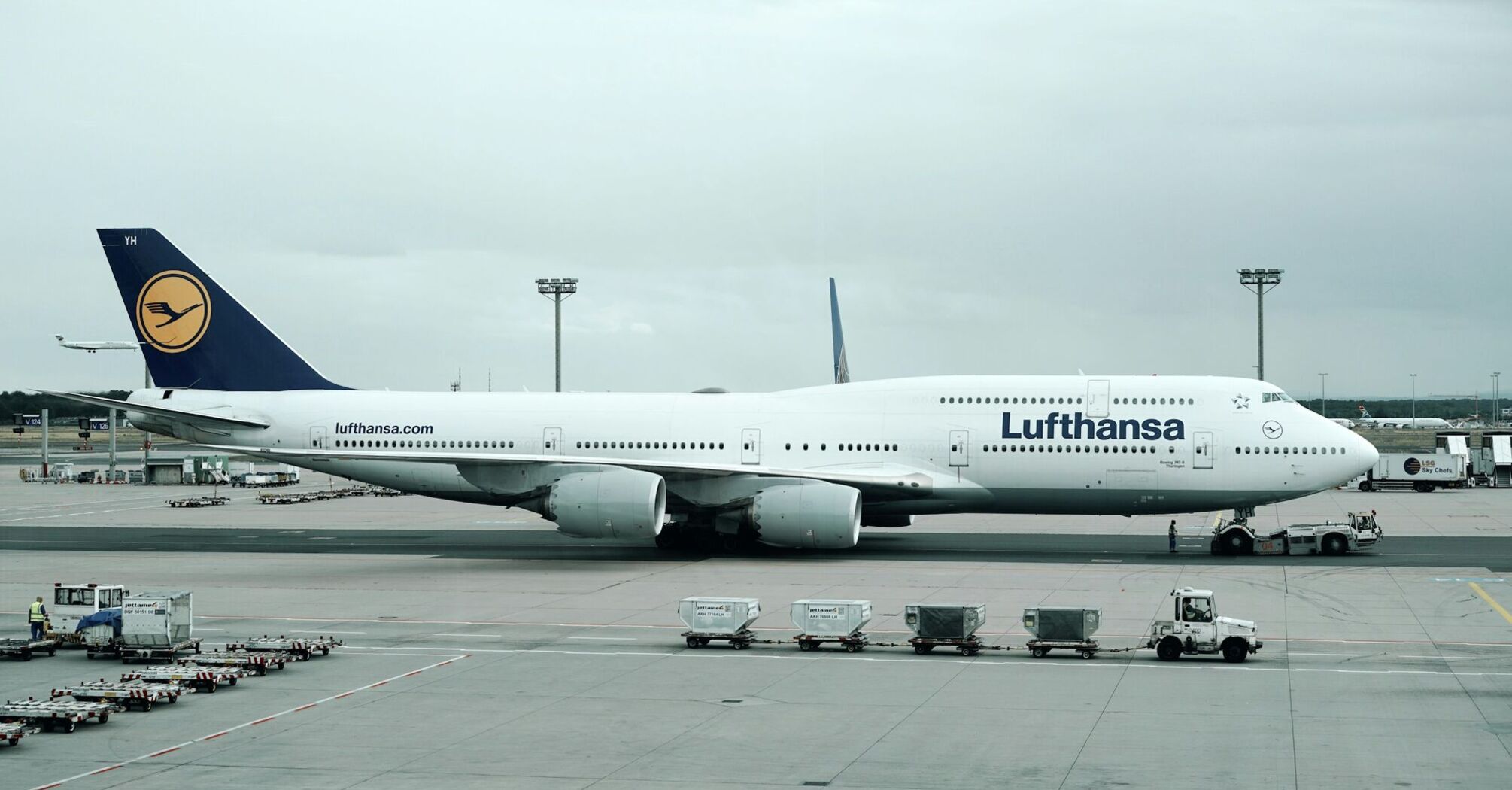 A Lufthansa aircraft parked at an airport gate, with ground support vehicles nearby