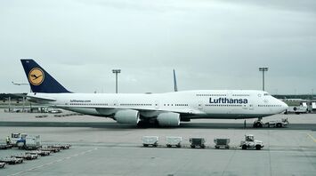 A Lufthansa aircraft parked at an airport gate, with ground support vehicles nearby