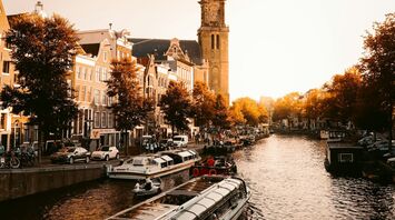A scenic canal in Amsterdam with a glass-roofed tour boat and the historic Westerkerk tower in the background during golden hour
