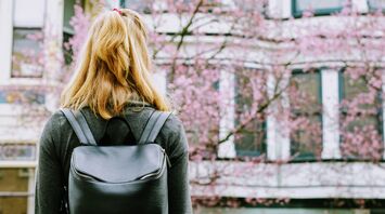 Woman with a backpack looking at cherry blossoms in front of a European-style building