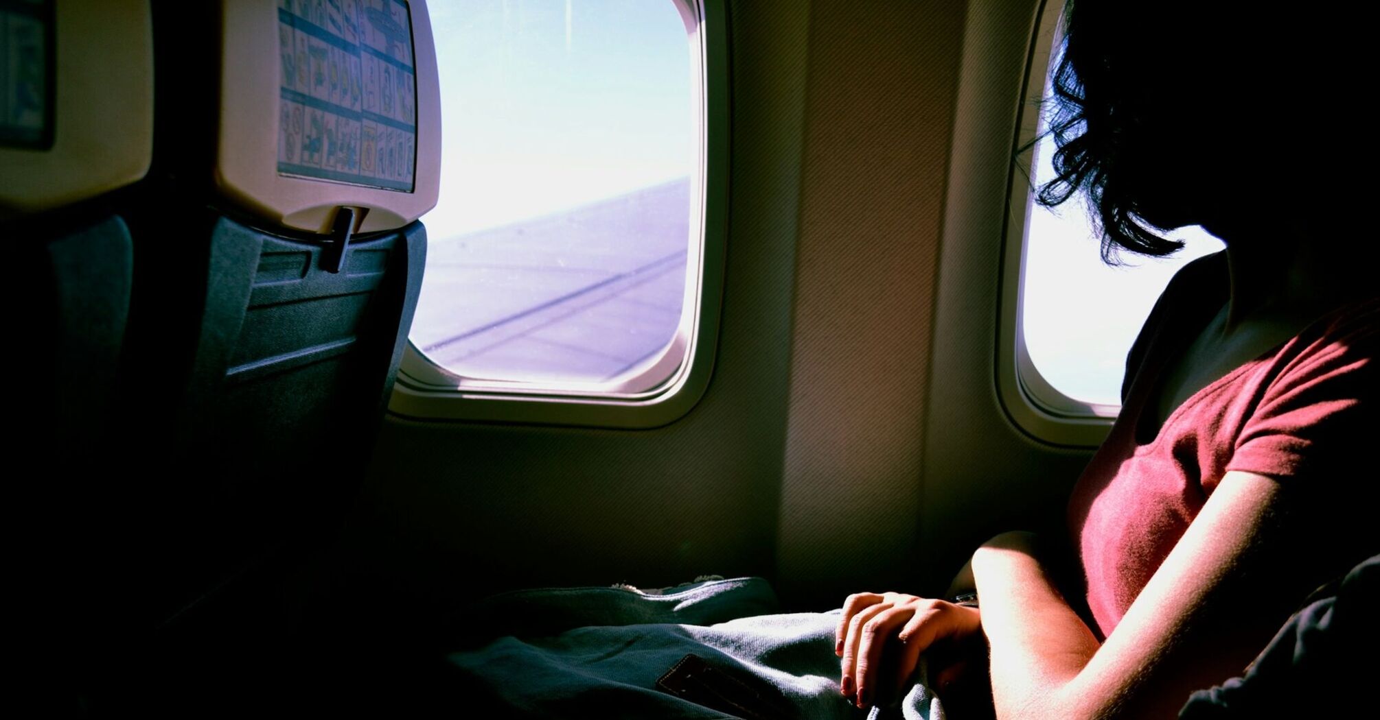 A solo traveler sitting by an airplane window with a backpack on their lap, gazing outside