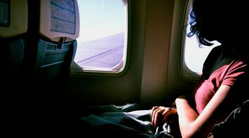 A solo traveler sitting by an airplane window with a backpack on their lap, gazing outside