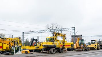A row of yellow construction vehicles and machinery near railway tracks during maintenance work