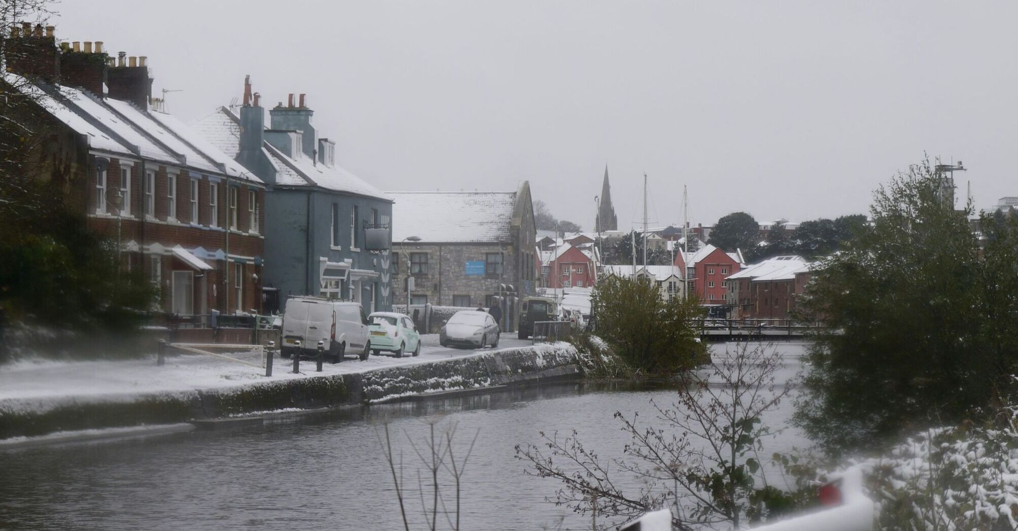 Snow-covered canal-side street with parked cars and historic buildings in winter