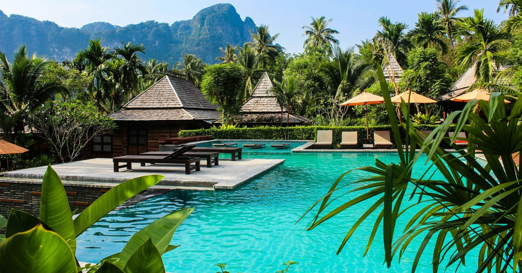 A luxury resort in Thailand with a tropical pool, wooden villas, and lush greenery in the background