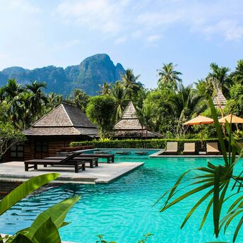 A luxury resort in Thailand with a tropical pool, wooden villas, and lush greenery in the background