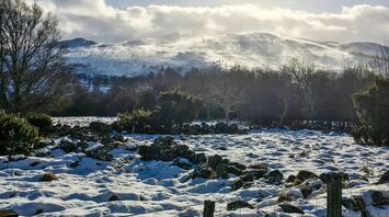 A snow-covered landscape in Scotland with hills in the background and scattered rocks in the foreground under a partly cloudy sky