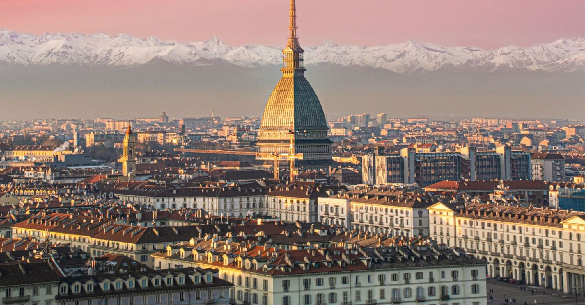 A scenic view of Torino with the Mole Antonelliana in the foreground and snow-capped Alps in the background during sunset