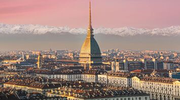 A scenic view of Torino with the Mole Antonelliana in the foreground and snow-capped Alps in the background during sunset