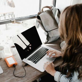 A woman working on a laptop near a window with a backpack on the table