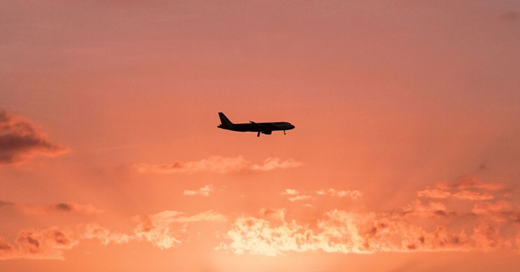 Airplane flying over the ocean at sunset with a dramatic sky