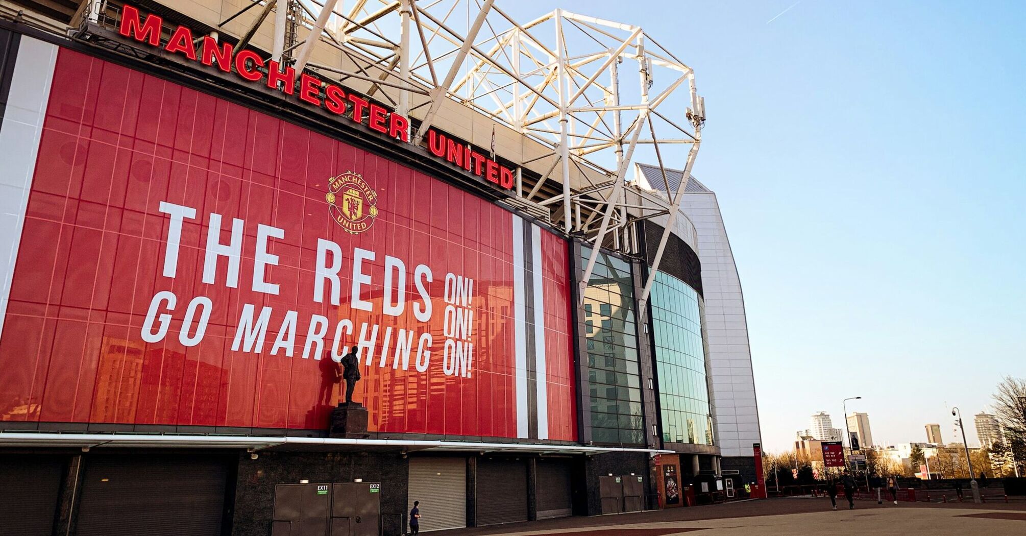 Old Trafford stadium with a large red banner displaying "The Reds Go Marching On!"