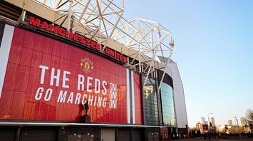 Old Trafford stadium with a large red banner displaying "The Reds Go Marching On!"